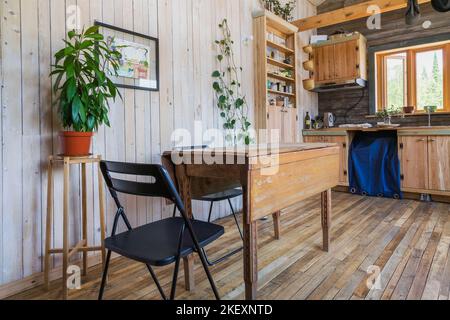 Table à manger en bois avec chaises pliantes, garde-manger en bois d'érable vieux de 100 ans et armoires dans le coin cuisine à l'intérieur rustique mini maison de 11,5 x 32 pieds. Banque D'Images