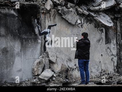 Borodyanka, Ukraine. 14th novembre 2022. Un homme prend une photo des graffitis du célèbre artiste anonyme de rue Banksy qui est montré sur l'un des immeubles d'appartements détruits par l'armée russe dans la ville de Borodyanka, au nord-ouest de la capitale ukrainienne Kiev. Banksy a posté une photo de graffiti d'un gymnaste faisant un stand sur son Instagram. Sur son Instagram, il ne publie que son propre travail. Crédit : SOPA Images Limited/Alamy Live News Banque D'Images