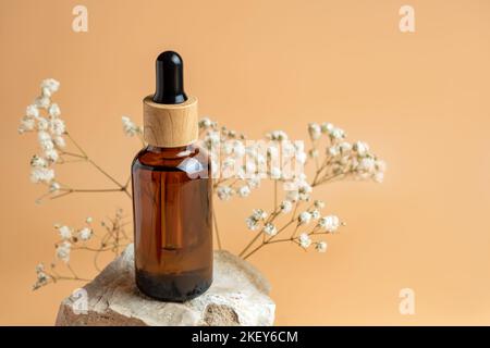 Concept esthétique minimaliste de soins de beauté. Bouteille de cosmétiques à base d'huile de sérum biologique en verre foncé sur pierre avec fleurs sur fond beige neutre Banque D'Images