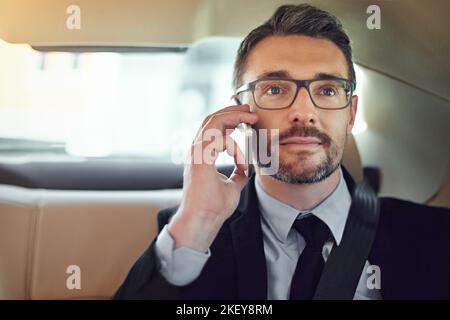 Faire des affaires en déplacement. Un homme d'affaires utilisant son téléphone portable tout en étant assis dans le siège arrière d'une voiture. Banque D'Images