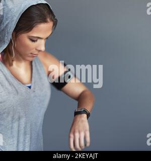 Un grand progrès. Une jeune femme sportive qui vérifie l'heure sur sa montre de sport sur fond gris. Banque D'Images