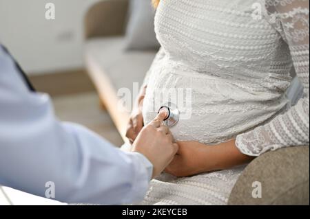 Femme médecin utilisant un stéthoscope pour écouter le rythme cardiaque du bébé dans le ventre d'une femme enceinte. Concept de maternité et de soins prénatals. Gros plan Banque D'Images