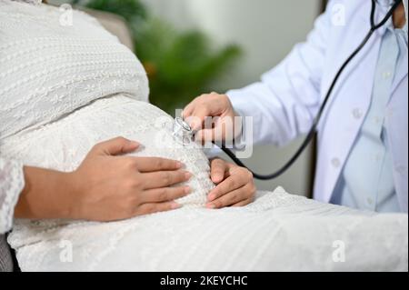 Gros plan et coupe courte, femme médecin ou obstétricien écoutant le rythme cardiaque de bébé par son stéthoscope. Concept de soins prénatals et de grossesse Banque D'Images