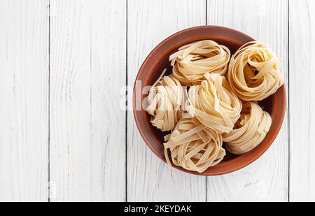 Pâtes tagliatelles non cuites dans un bol en céramique sur fond de bois blanc avec espace pour les copies Banque D'Images