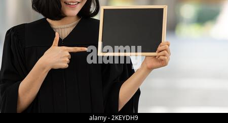 Jeune femme souriante tenant et pointant vers le tableau noir. Banque D'Images
