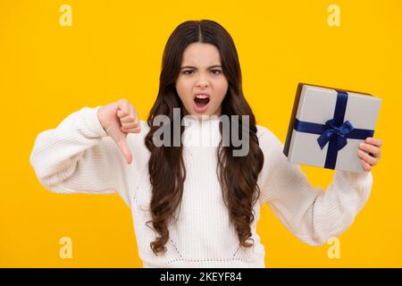 Visage en colère, émotions bouleversées de la jeune fille. Enfant jeune fille avec cadeau sur fond jaune isolé. Anniversaire, cadeau de vacances concept Banque D'Images