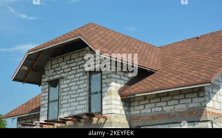 Construction de toitures avec bardeaux d'asphalte. Gros plan sur la construction de maison inachevée avec balcon grenier, fenêtres de mansarde, évents de toit, bardeaux d'asphalte Banque D'Images