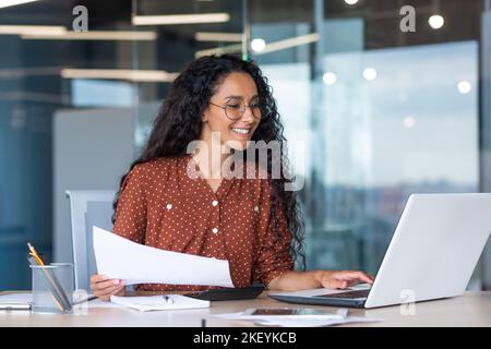 femme d'affaires latino-américaine travaillant au bureau avec des documents et un ordinateur portable, la paperasserie calcule des indicateurs financiers souriant et heureux avec le succès et les résultats de réalisation et de travail Banque D'Images