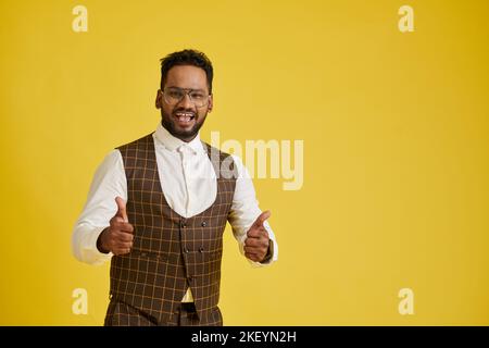 Joyeux homme excité en chemise blanche et gilet à carreaux montrant le pouce-vers le haut avec les deux mains Banque D'Images