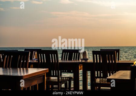 Rangée de tables et chaises en bois vintage d'un restaurant sur la plage de Thaïlande, pas de personnes, heure du coucher du soleil, fond flou de la mer et du ciel. Spa vierge Banque D'Images