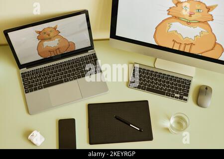 Vue au-dessus de l'ordinateur portable et de l'ordinateur avec chat rouge gras sur les écrans sur le lieu de travail de l'artiste numérique avec des gadgets mobiles et des appareils de bureau Banque D'Images