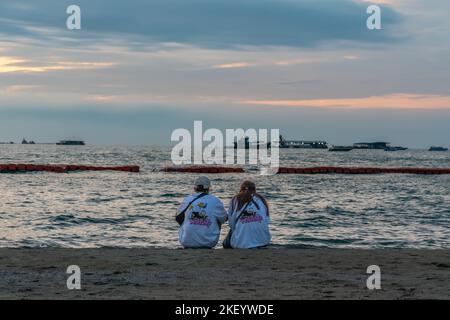 Couple assis près de la plage et profitant de la vue sur le coucher du soleil à Pattaya, Thaïlande. Tir horizontal, Banque D'Images