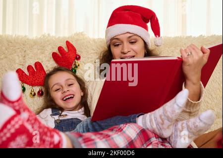 Famille heureuse, mère aimante et fille appréciant des moments heureux en lisant des contes de fées pendant les vacances de Noël à la maison Banque D'Images