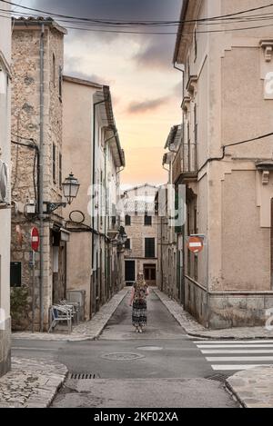 Vue arrière de la femme en robe longue debout au milieu d'une rue étroite au milieu de maisons historiques dans la vieille ville espagnole de Soller Banque D'Images