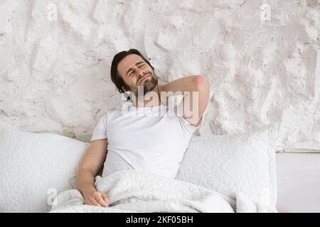 Triste homme de race blanche millénaire désespéré avec un chaume maque son cou sur un lit blanc aux couvertures et souffre de mal Banque D'Images