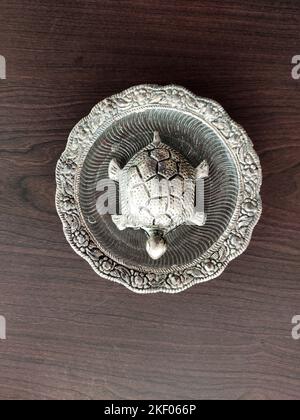 Une vue en haut d'une figurine de tortue plaquée argent reposant sur une surface en bois, mettant en valeur son design complexe contre le riche grain du bois. Banque D'Images