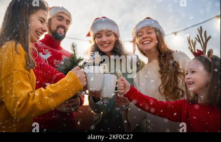 Des amis heureux fêtent Noël en plein air. Les adultes et les enfants s'amusent en portant des chapeaux de père Noël. Banque D'Images