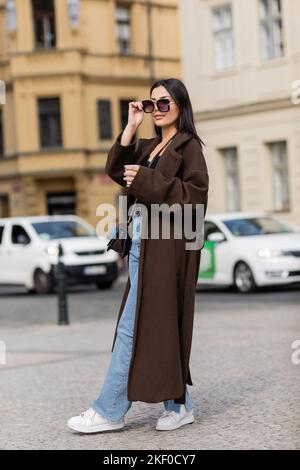 Jeune touriste élégant tenant une tasse en papier et des lunettes de soleil dans la rue à Prague, image de stock Banque D'Images