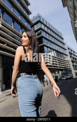 Femme souriante tatouée marchant dans la rue urbaine avec le soleil à Prague, image de stock Banque D'Images