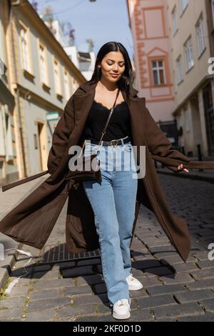 Femme souriante en manteau marchant sur la route dans la rue urbaine de Prague, image de stock Banque D'Images