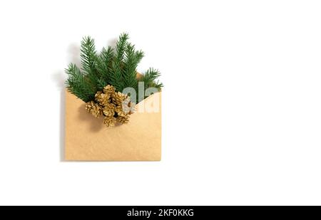 Brindilles d'épinette et cônes dorés dans une enveloppe artisanale isolée sur un fond blanc. Carte de vœux de Noël. Lettre du nouvel an. Espace de copie, vue de dessus, plat Banque D'Images