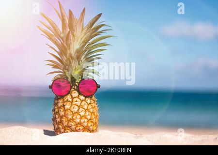 Ananas tropical créatif dans des lunettes de soleil roses sur une plage de sable Banque D'Images