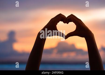 Mains formant un coeur avec silhouette de coucher de soleil Banque D'Images