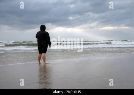Personne debout sur la plage le jour nuageux. La côte de mer après la tempête avec la femme regardant l'horizon. Banque D'Images