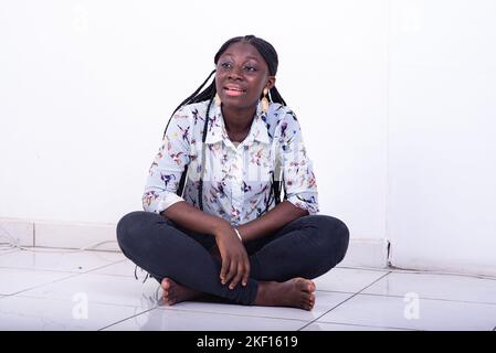 une jeune femme dans une chemise assise sur le sol sur un fond blanc parlant à quelqu'un. Banque D'Images