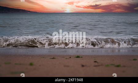 Coucher de soleil coloré sur la plage tropicale, le soleil derrière les nuages se reflète sur l'eau et les vagues avec de la mousse frappant le sable. Mise au point sélective. Copier pour le texte. Banque D'Images