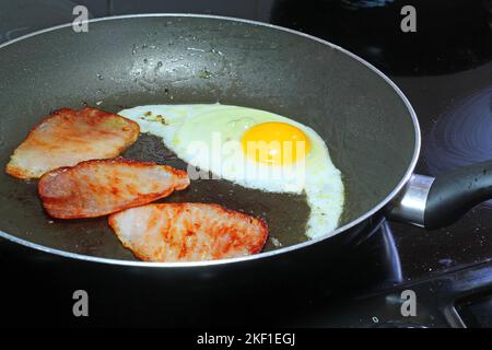 Œufs et trois tranches de bacon frits dans une poêle pour le petit déjeuner. Banque D'Images