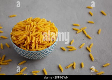 Mini-pâtes de Penne maison à sec dans un bol sur fond gris, vue latérale. Banque D'Images