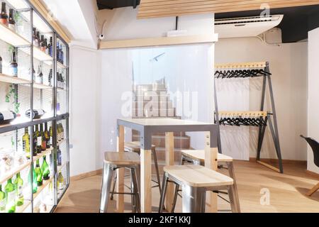 Une salle de restaurant avec de hautes tables et chaises en bois et une étagère avec des bouteilles de vin Banque D'Images