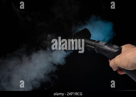 Nettoyage à la vapeur à la maison. Vapeur sur fond noir. Banque D'Images