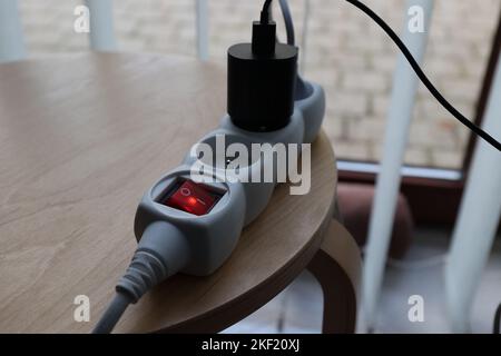 Un portrait d'une multiprise blanche avec un bouton marche/arrêt rouge et un chargeur noir. Les prises de l'appareil sont allumées et le voyant s'allume dans le bu Banque D'Images