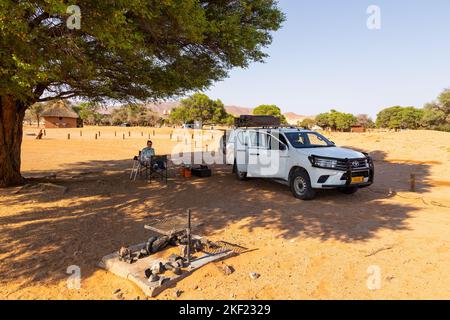Camping Sesriem, Sossusvlei, Namibie - 01 octobre 2018 : une fille assise sous un acacia au camping. Voiture avec équipement garé à proximité. Banque D'Images