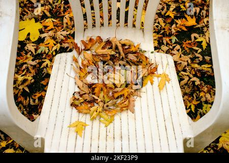 Les feuilles tombées en automne s'accumulent sur une ancienne chaise de pelouse en plastique dans la cour arrière Banque D'Images