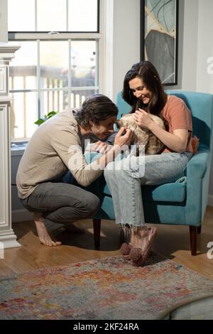 Un homme et une femme dans leur salon avec leur chat, se blottant avec amour dans une chaise bleue. Banque D'Images