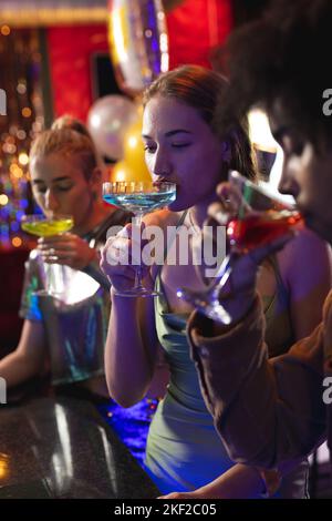 Trois amis hommes et femmes heureux et variés sirotant des cocktails au bar de la discothèque Banque D'Images