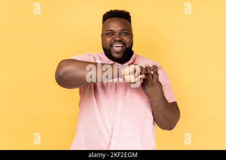 Portrait d'un homme populaire blogueur portant une chemise rose faisant un hashtag signe avec les doigts, regardant l'appareil photo avec le sourire, marquant des postes dans les réseaux sociaux. Studio d'intérieur isolé sur fond jaune. Banque D'Images