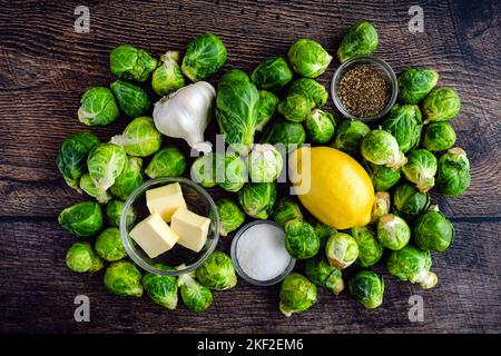 Choux de Bruxelles rôtis au beurre d'ail Ingrédients sur un fond de bois : choux de Bruxelles crus, ail et autres ingrédients pour un plat d'accompagnement Banque D'Images