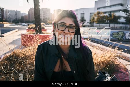 brunette latina fille avec des verres perce des lèvres boucles d'oreilles veste de fourrure assis dans la ville regardant l'appareil photo Banque D'Images