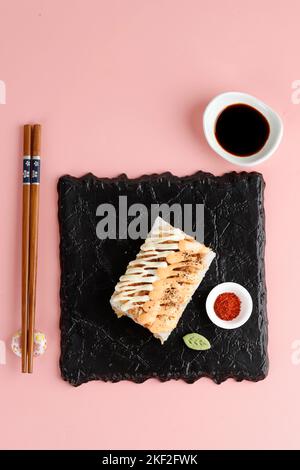 Mini-sushi japonais avec garniture de mayonnaise servi sur une assiette de ardoise noire, sur fond rose. Mise au point sélectionnée Banque D'Images