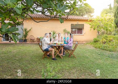 Photo d'amis mangeant et buvant dans le patio. Personnes d'âge moyen et gaies autour de la table. Banque D'Images