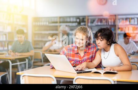 Portrait d'une écolière asiatique avec une amie espagnole qui étudie à la bibliothèque à l'aide d'un ordinateur portable Banque D'Images