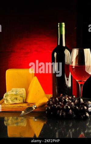 Table avec un mélange de différents fromages, bouteille et verre de vin à proximité Banque D'Images