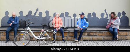 PRODUCTION - 11 novembre 2022, Saxe, Mügeln: Sur le marché de la petite ville du nord de la Saxe, également connue sous le nom de "centre bancaire", deux hommes et deux femmes sont assis sur la très longue "Volksbank", derrière laquelle les silhouettes de 16 personnes peuvent être vues. Depuis 2009, des bancs conçus avec imagination ont été placés dans toute la ville sous la direction du 'conseil de surveillance bancaire'. Au début du mois de décembre, la banque 50th sera officiellement incluse dans le « Centre bancaire ». (À dpa 'The 'Bank Centre' Mügeln Gs') photo: Waltraud Grubitzsch/dpa Banque D'Images