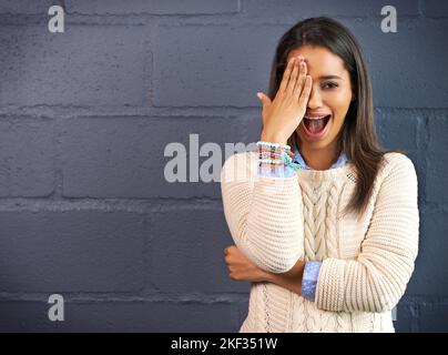 Garder un demi-oeil sur les choses. Une jeune femme couvrant son oeil contre un fond de mur de brique. Banque D'Images