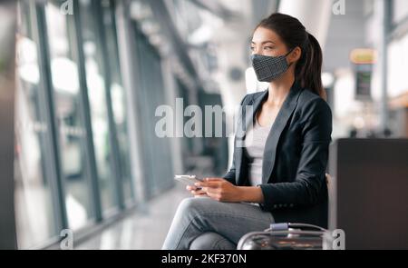 Voyager pendant le coronavirus. Femme d'affaires asiatique portant un masque facial dans le terminal de l'aéroport attendant un vol pensant regarder par la fenêtre à l'aide du téléphone Banque D'Images