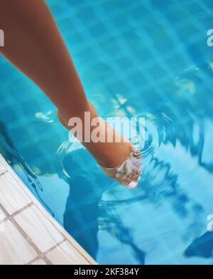 Des eaux accueillantes. Une femme qui s'arrose ses pieds dans l'eau d'une piscine. Banque D'Images